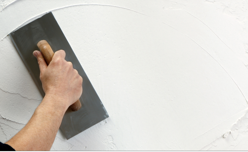Hand with trowel plastering a white wall